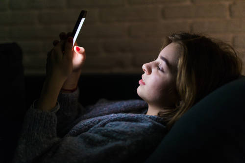 Young beautiful woman using smart phone at night in bed - technology, social network, insomnia concept